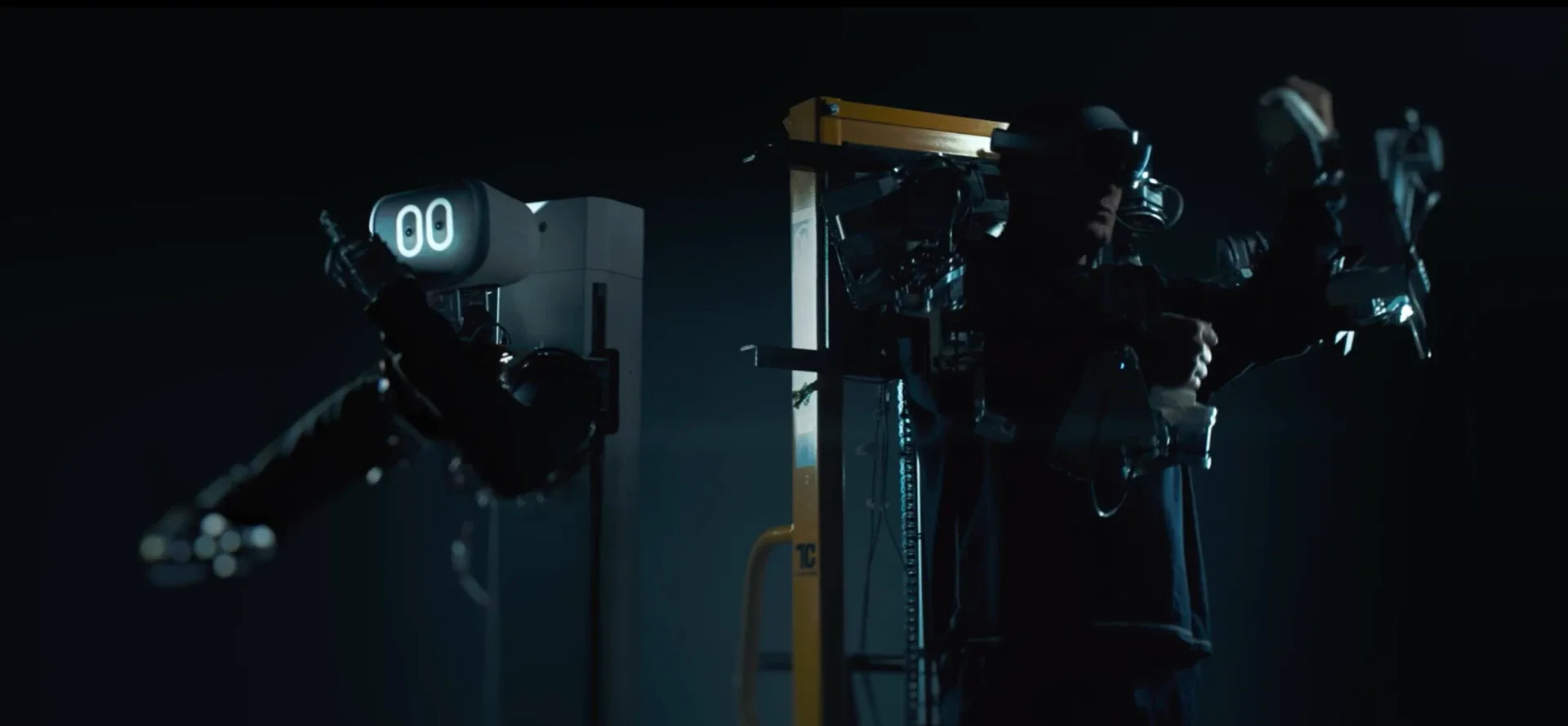An operator in the exoskeleton and headset drives the Mundane robot, which raises its arm to mirror the operator